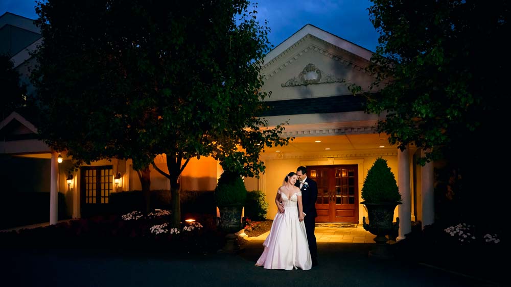 During blue hour the bride and groom embracing in front of Bradford Estate wedding venue in Hainsport NJ.