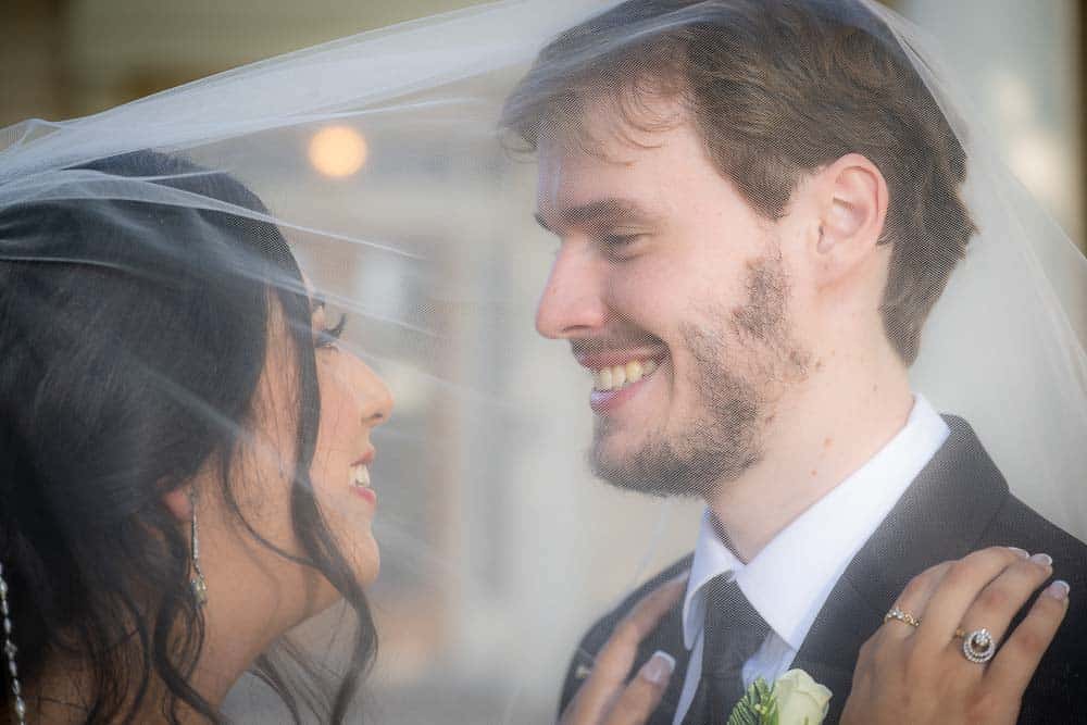 Both the groom and bride underneath the brides veil at the Collingswood Grand Ballroom Wedding.