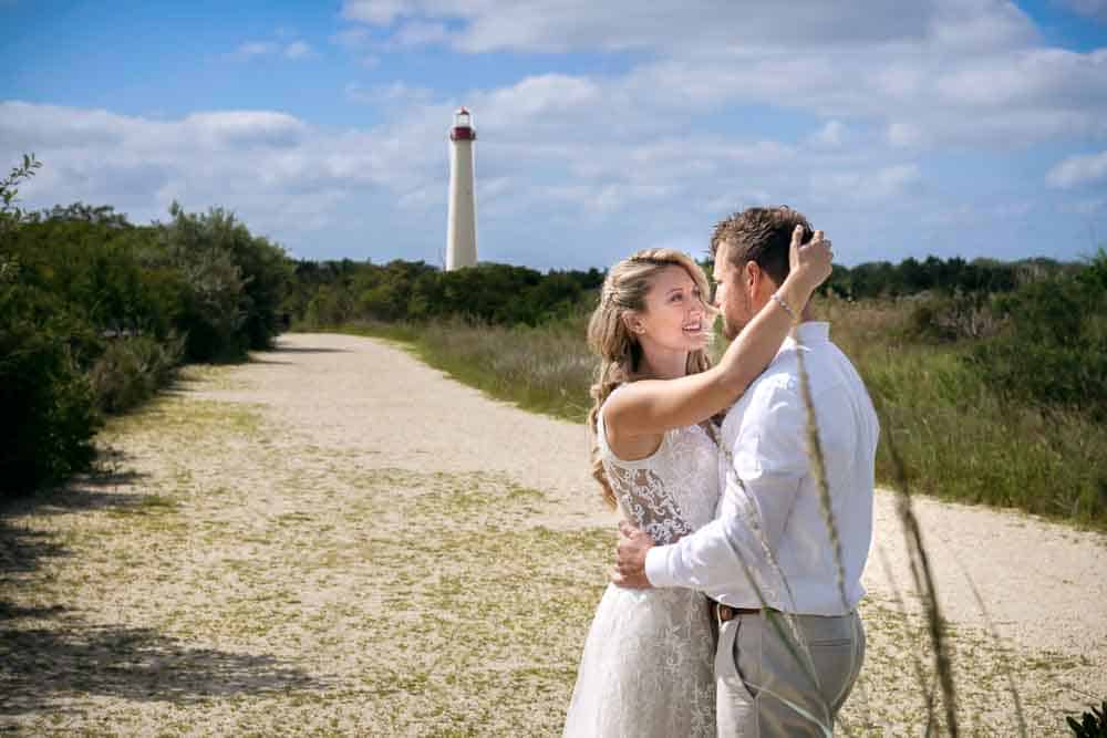 Couple embracing each other with the Cape May lighthouse in the background.