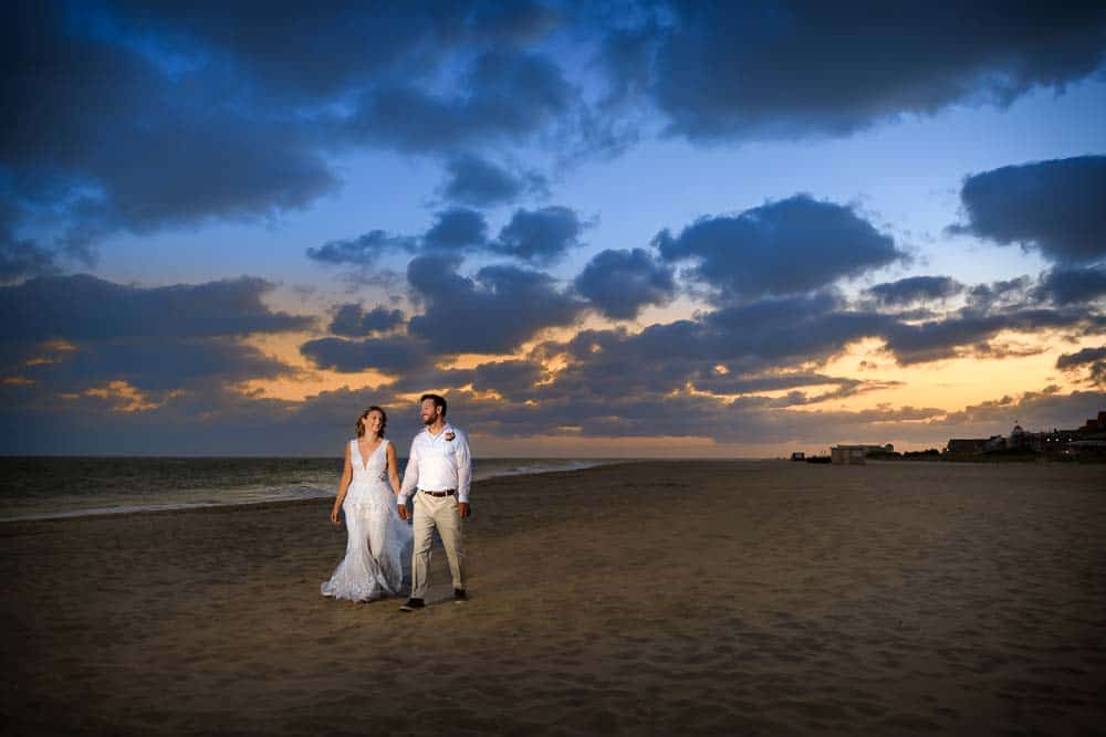 bride and groom strolling on the beach by the Grand Hotel of Cape May