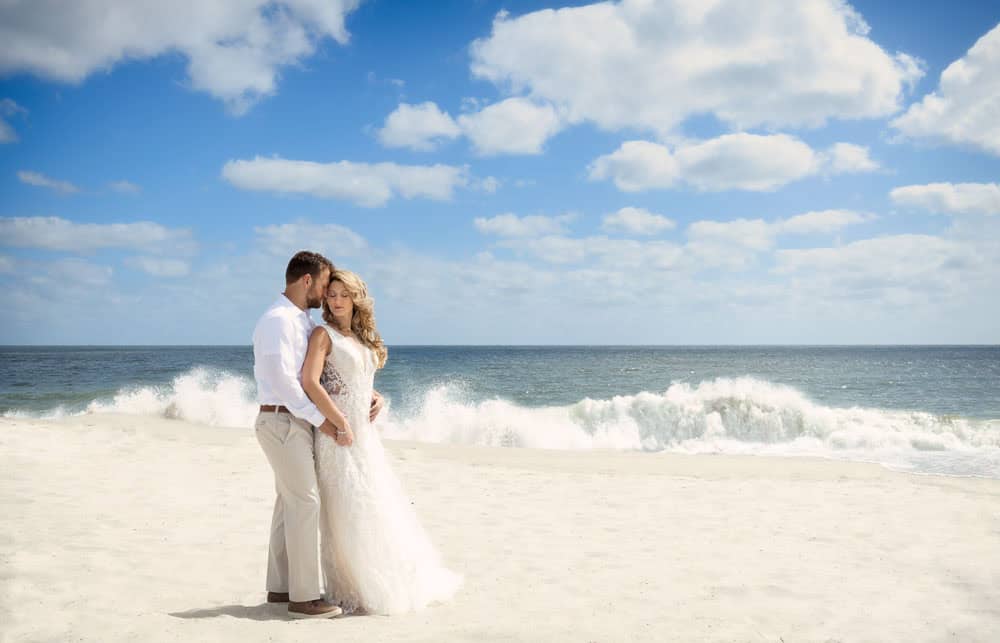 beautiful ocean crashing onto the shore with a bride and groom standing on the beach