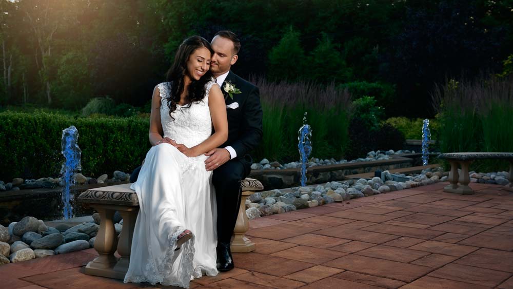 Couple embracing each other by the small fountain in front of the Chapel at Brigalias Sicklerville NJ.