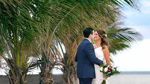 Bride and groom embracing by the palm trees at ICONA Diamond Beach Wedding.