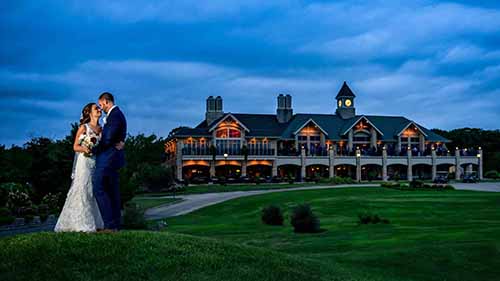 Bride and groom embracing on the hill during the evening with the Scotland Run Country Club wedding venue in the background.