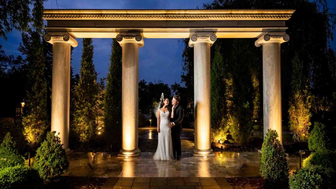 Bride and Groom embracing underneath grand columns during sunset at Mansion on Main Street in Voorhees NJ